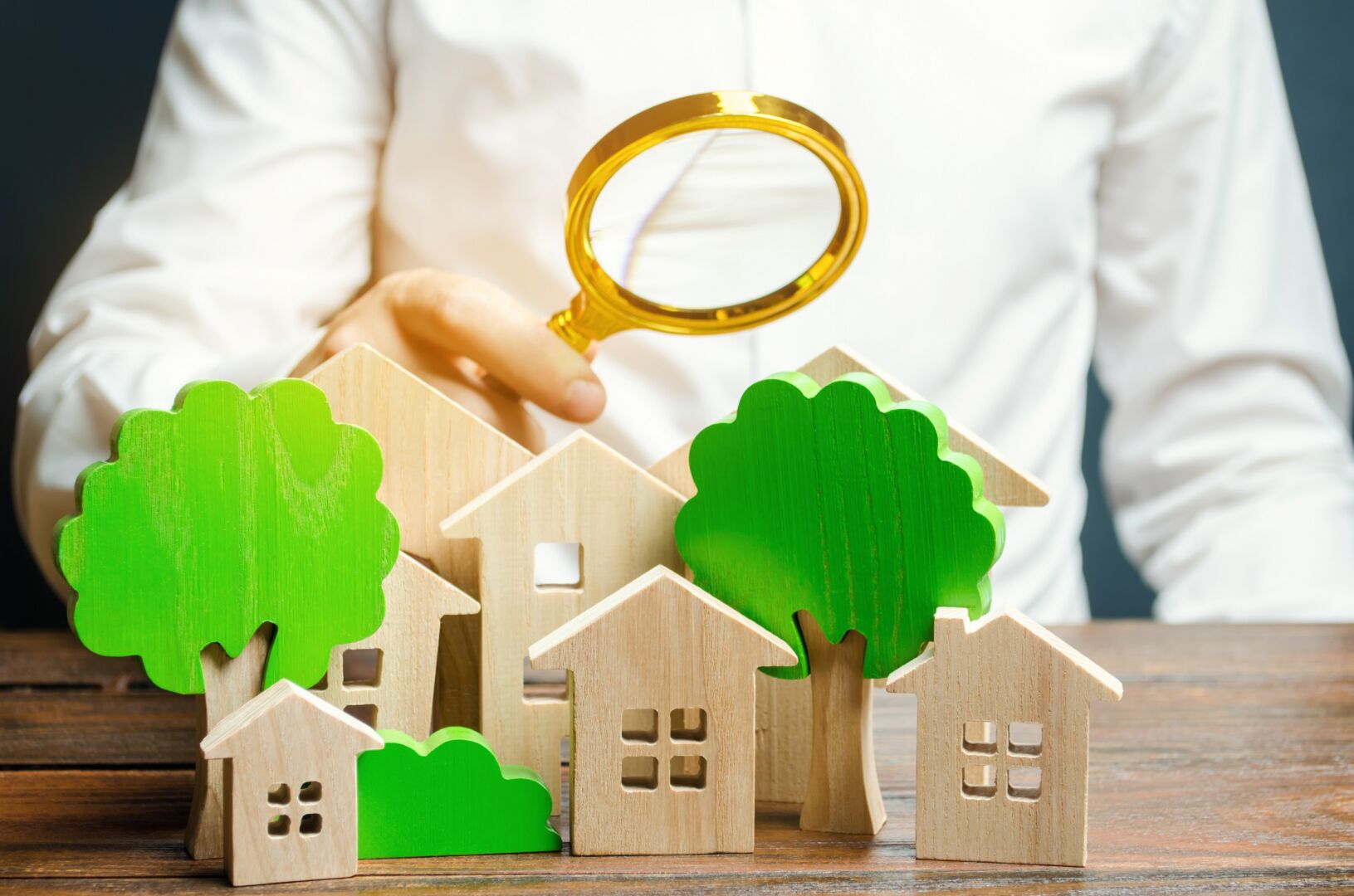 photo : A man holds a magnifying glass over wooden houses and trees. Real estate valuation and selection of a place for the construction of new buildings. Evaluation of urbanism and residential space.
