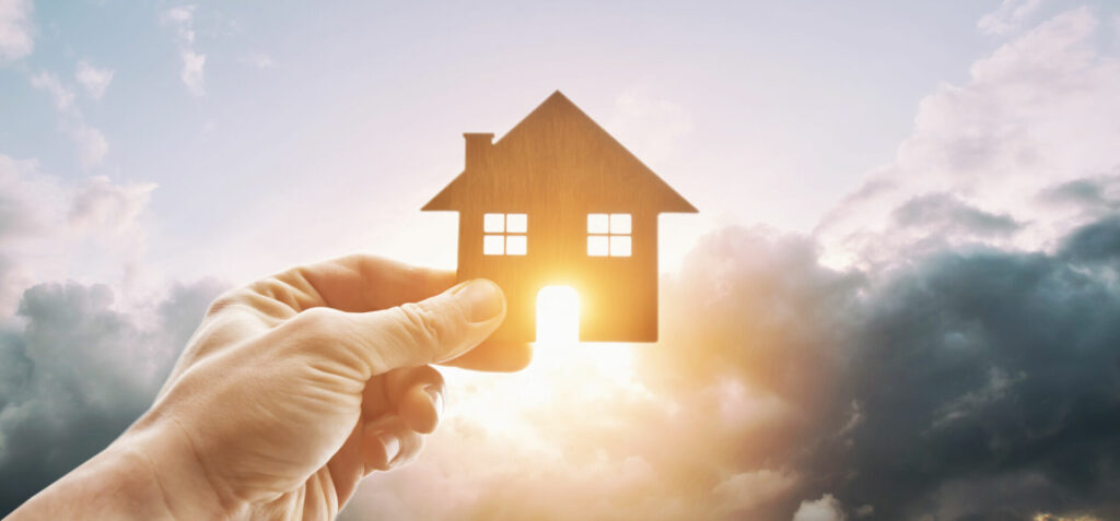 photo : Man's hand holds wooden flat house against the sun