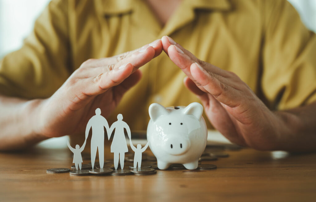 photo : Businessman take a position to protect on the piggybank and paper family in hand, donation, saving, charity, family finance plan concept, fundraising, superannuation, financial crisis concept