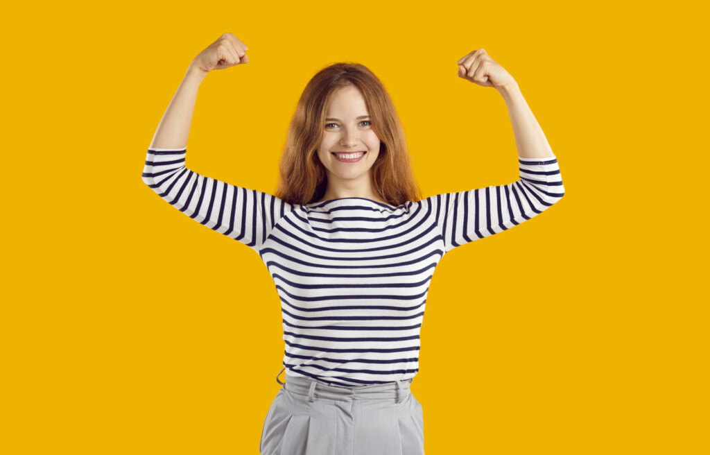 photo : Happy confident beautiful young woman smiling, flexing her arms and showing girl power