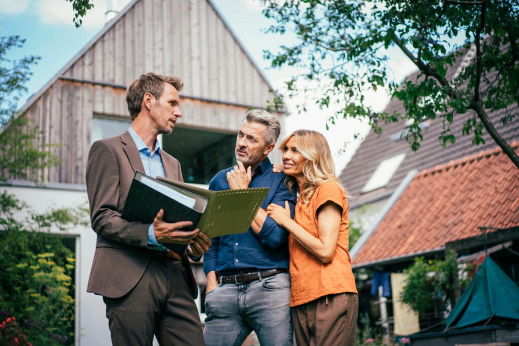photo : Mature couple discussing over documents with real estate agent in front of house