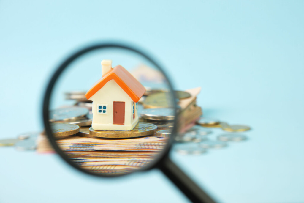 photo : Miniature house and money under a magnifying glass. Concept of real estate investment, mortgage, home insurance, home purchase and sale.